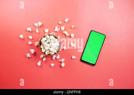 Draufsicht auf Smartphone und Popcorn auf rotem Hintergrund Stockfoto