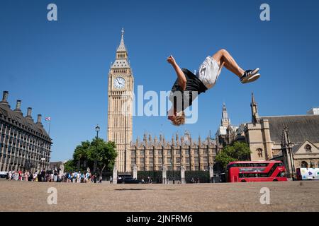 Der Trampolinist Johannes Luethi aus Österreich übt einige Bewegungen auf einem ausgetrockneten Parliament Square im Zentrum von London aus, nachdem er an der Freestyle Trampolin World Championships in Hackney, Ost-London, teilgenommen hat. Das Met Office hat zwischen Donnerstag und Sonntag eine bernsteinfarbene Hitzewarnung herausgegeben, bei der die Temperaturen in Südengland und im Osten von Wales auf 36C steigen könnten, wobei einige Gebiete mit einem „außergewöhnlichen“ Risiko von Waldbränden konfrontiert sind, da der Fire Severity Index auf seinen höchsten Wert angehoben wird. Bilddatum: Donnerstag, 11. August 2022. Stockfoto