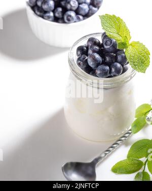 Gesundes Frühstück im Sommer. Naturjoghurt im Glas mit frischen Waldbluebeeren. Weißer Hintergrund. Heidelbeere ist sehr reich an Vitaminen. Natürliches Supe Stockfoto