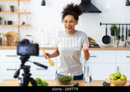 Junge Frau, die Salat in der heimischen Küche zubereitet schöne Frau, die mit der Kamera ein Video über gesundes Kochen aufzeichnet Stockfoto