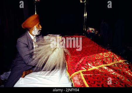 Southall London England Mann beim Lesen des Sri Guru Granth Sahib & Romalla Stoffes oben mit einem Chauri in Gurdwara Stockfoto