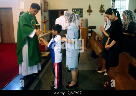 Priester, der bei der koreanischen Messe die katholische Kirche St. Anne in Kingston, England, zur Kommunion gibt Stockfoto