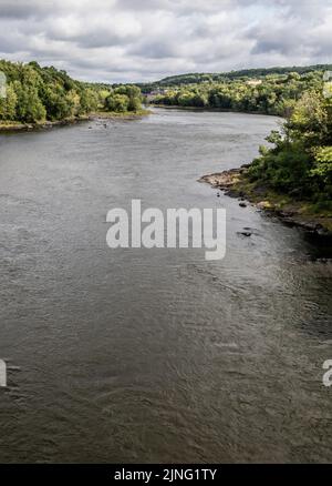 St. Croix River mit üppigen grünen Bäumen, die das Wasser umsäumen, beleuchtet durch das Sonnenlicht unter einer wunderschönen Wolkendecke. Stockfoto