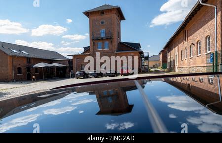 11. August 2022, Sachsen, Stollberg: Das alte Schlachterhaus in Stollberg spiegelt sich in einem Autodach wider. Heute wird das Industriegebäude als Veranstaltungsort für Konzerte, Workshops und Projekte genutzt. Die Stadt, die rund 11.500 Einwohner hat und an der Autobahn 72 liegt, hat eine Reihe von Beispielen dafür, wie Millionen von Bundes- und Landesmitteln verwendet wurden, um neue Dinge zu schaffen oder alte Gebäude zu renovieren und neu zu nutzen. Seit Anfang des Jahres 1990s flossen von Bund und Ländern rund 6,2 Milliarden Euro in die sächsischen Städte zur Stadtsanierung. Foto: Hendrik Schm Stockfoto