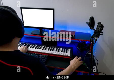 Rückansicht eines männlichen Tontechnikers mit Kopfhörern, der das elektrische Klavier spielt und in seinem Heimstudio Musik mischt und aufnimmt Stockfoto