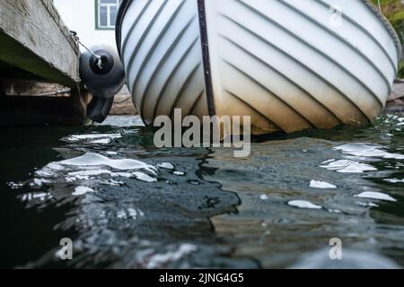 Das Boot ist an einem alten hölzernen Pier mit einem Schwimmer an der Küste festgemacht. Nahaufnahme. Stockfoto