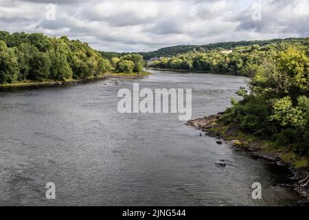 St. Croix River mit üppigen grünen Bäumen, die das Wasser umsäumen, beleuchtet durch das Sonnenlicht unter einer wunderschönen Wolkendecke. Stockfoto