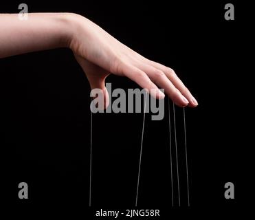 Manipulation, Missbrauchskonzept. Weibliche Hand ziehen Saiten auf schwarzem Hintergrund. Stockfoto