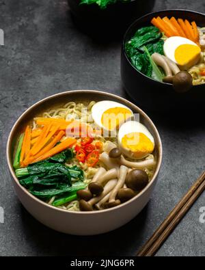 Asiatische Nudeln Suppe mit Pilzen, Eiern, dan sortiertes Gemüse auf dunklem Hintergrund. Stockfoto
