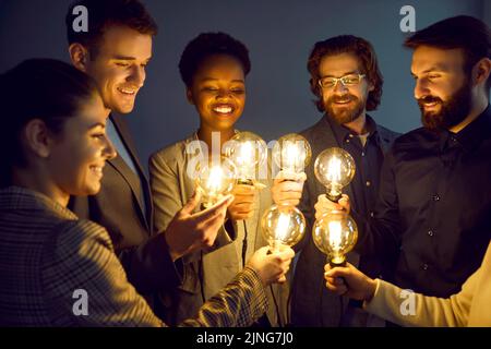 Eine Gruppe glücklicher intelligenter Menschen hält helle, leuchtende Glühbirnen als Symbol für kreative Ideen. Stockfoto