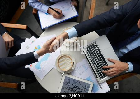 Geschäftsleute schütteln sich die Hände übertrieben mit Dokumenten Stockfoto