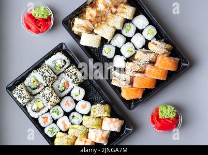 Große Sushi-Rollen in schwarzer Plastikbox zum Mitnehmen auf grauem Hintergrund. Draufsicht Stockfoto