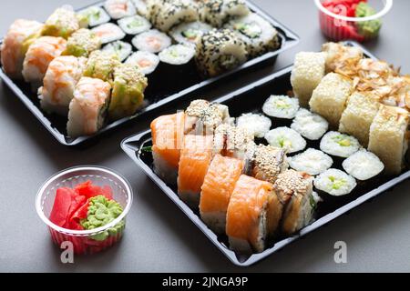 Große Sushi-Rollen in schwarzer Plastikbox zum Mitnehmen auf grauem Hintergrund Stockfoto