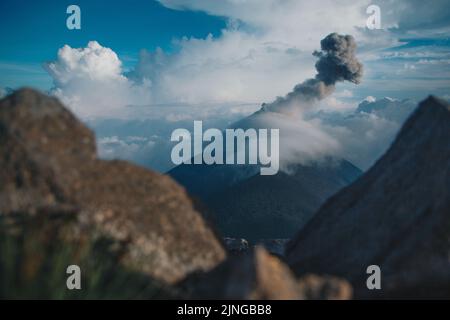 Eine Eruption des Volcan de Fuego, bedeckt von kalten Wolken, bevor sich ein Gewitter dem Sonnenuntergang nähert. Stockfoto