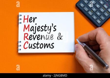 HMRC her majestys Einkommens- und Zollsymbol. Konzeptworte HMRC her majestys Einnahmen und Bräuche auf weißer Note auf schönem orangenen Hintergrund. Bus Stockfoto