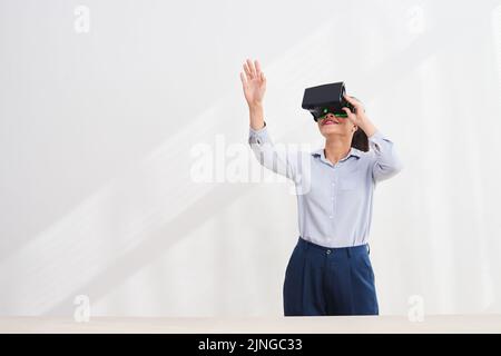 Fröhliche junge Frau mit einer Vr-Brille, die ihre Hand ausstreckt Stockfoto