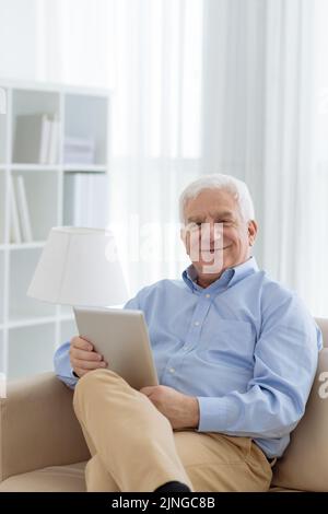 Porträt eines glücklichen, gealterten Mannes mit digitalem Tisch, der im Armschir sitzt Stockfoto