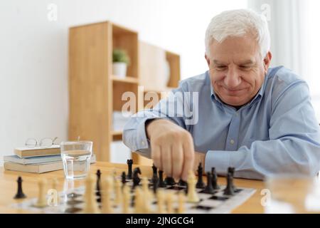 Ein älterer lächelnder Mann spielt gerne Schach im Pflegeheim Stockfoto