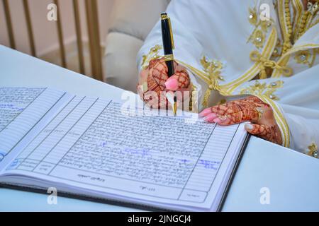 Eine arabische Braut unterzeichnet ihren Ehevertrag mit Henna-Tattoos auf ihren Händen Stockfoto
