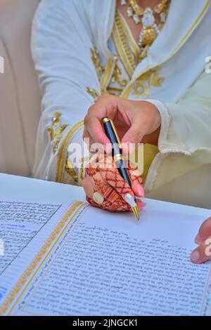 Eine arabische Braut unterzeichnet ihren Ehevertrag mit Henna-Tattoos auf ihren Händen Stockfoto