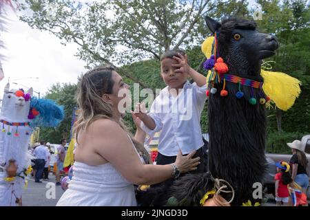 Eine Verkäuferin und ihr Sohn an einem Stand mit einer hölzernen Tierstatue. Bei der ecuadorianischen Parade NYC 2022 in Jackson Heights, Queens, New York City. Stockfoto