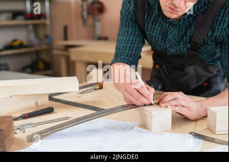 Ein Zimmermann mißt Holzbohlen und macht in einer Werkstatt mit einem Bleistift Markierungen. Stockfoto