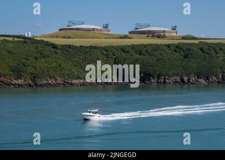 Ein Schnellboot fährt mit hoher Geschwindigkeit entlang und lässt eine Wake hinter sich, mit Blick auf die Ölbehälter von Milford Haven hinter sich in Südwales Stockfoto