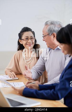Fröhliches asiatisches Paar, das mit einem talentierten Designer über ein Innenraumprojekt spricht und sich im geräumigen Studio produktiv trifft Stockfoto