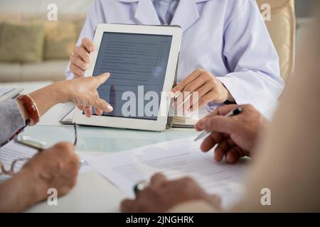 Nahaufnahme des älteren Ehepaares, das in der Arztpraxis saß und eine medizinische Form ausfüllte, Ärztin mit weißem Mantel, die ihnen half Stockfoto