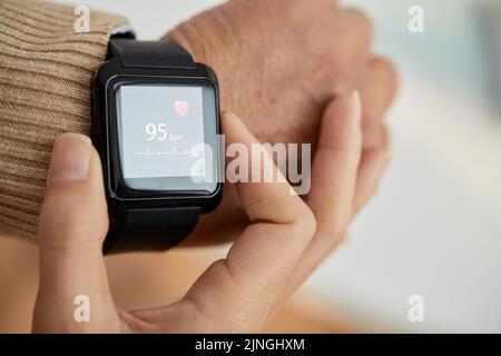 Nahaufnahme einer nicht erkennbaren Ärztin, die den Puls ihrer älteren Patientin mithilfe einer Smart Watch und eines verschwommenen Hintergrunds überprüft Stockfoto