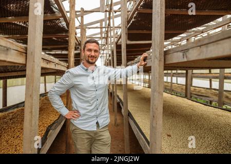 Lächelnder Manager posiert zwischen hohen Holzregalen auf der Kaffeefarm Stockfoto