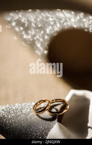 Zwei goldene Ringe liegen auf Hochzeitsschuhen. Stockfoto