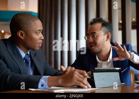 Multiethnische Geschäftspartner diskutieren bei Treffen im Restaurant über verschiedene Themen Stockfoto