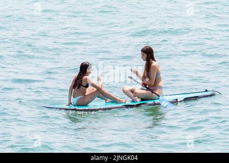 Tel Aviv, Israel. 10. August 2022. Teenager werden beim Schwimmen auf einem Surfbrett in Tel Aviv mit ihrem Telefon gesehen. Tel Aviv, das sich an der Mittelmeerküste befindet, ist Israels kulturelles Zentrum und ein wichtiges Reiseziel, das Touristen aus der ganzen Welt anzieht. (Bild: © Ronen Tivony/SOPA Images via ZUMA Press Wire) Stockfoto
