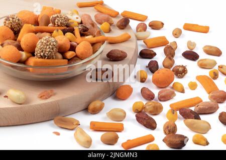 Gemischte geröstete Nüsse und Erdnüsse, geschält in einer Glasschale, gegen ein Holzbrett. Nahaufnahme. Stockfoto