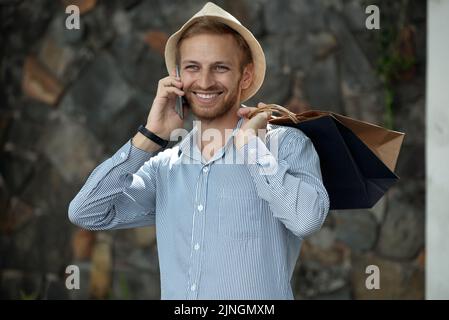 Glücklicher Mann mit Einkaufstaschen, der sich am Handy unterhielt Stockfoto