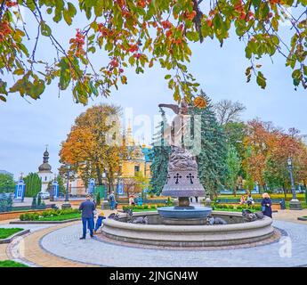 KIEW, UKRAINE - 9. NOV 2022: Der Brunnen des Erzengels Michael im farbigen Herbstpark des Wolodymyr-Hügels mit einem Gebäude der Goldenen Kuppel des Heiligen Michael Stockfoto