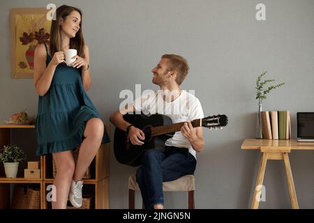 Glücklicher junger Mann spielt Gitarre für seine schöne Freundin Stockfoto