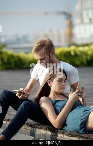 Junges Paar mit Smartphones, während sie sich gemeinsam im Freien entspannen Stockfoto