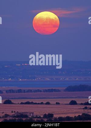 Eastchurch, Kent, Großbritannien. 11. August 2022. UK Wetter: Der volle Sturgeon Mond - der letzte Supermond des Jahres 2022 - wurde heute Abend in Eastchurch, Kent, über ausgetrocknten Feldern aufsteigen sehen. Kredit: James Bell/Alamy Live Nachrichten Stockfoto