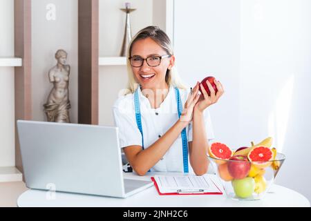 Porträt einer jungen lächelnden Ernährungsberaterin im Sprechzimmer. Ernährungsberater mit gesundem Obst, Saft und Maßband. Diätassistent arbeitet Stockfoto