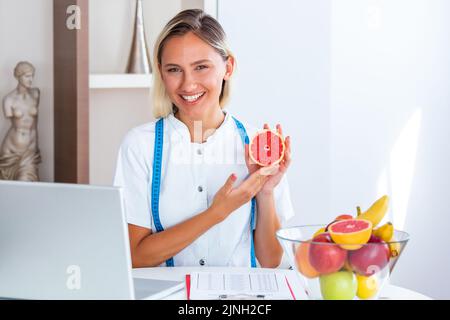 Porträt einer jungen lächelnden Ernährungsberaterin im Sprechzimmer. Ernährungsberater mit gesundem Obst, Saft und Maßband. Diätassistent arbeitet Stockfoto