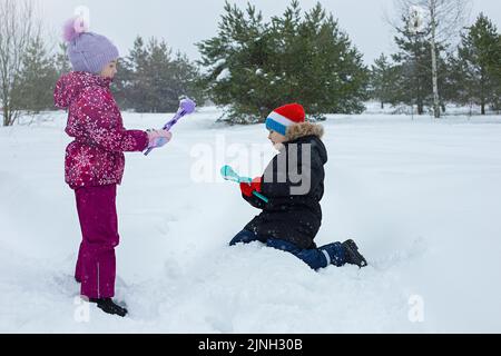 Ein Junge und ein Mädchen sind im Winter draußen und machen Schneebälle mit Plastikmodellierwerkzeugen. Stockfoto