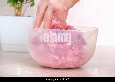 Ein Mann mischt Hackfleisch in einer Schüssel mit seinen Händen. Zubereitung von Hackfleisch und Schweinefleisch für Koteletts, Fleischbällchen, Koteletts. Stockfoto