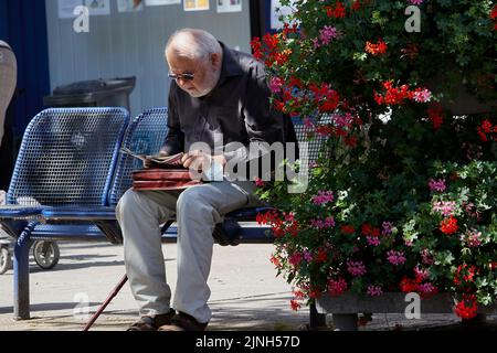 Ein alter Mann mit Sonnenbrillen liest ein Magazin auf einer Bank in Heinsberg, Deutschland Stockfoto