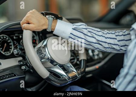 Nahaufnahme der männlichen Hand, die das Lenkrad eines Luxuswagens hält. Stockfoto