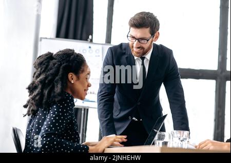 Verhandlungen zweier intelligenter Mitarbeiter. Erfolgreiche Geschäftskollegen, kaukasischer Mann und afroamerikanische Frau, im modernen Büro, diskutieren neues Projekt, Finanzgeschäftsplan, zukünftige Strategie Stockfoto