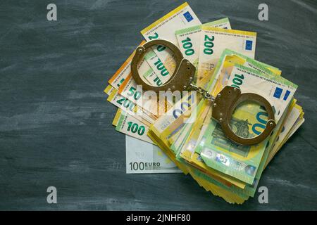 Handschellen, Euro-Rechnungen auf schwarzem schwarzen Tafel Hintergrund. Economic crimes.Arrest auf Bankkonten und Eigentum. Korruption und Verschwendung des Haushalts in der Stockfoto