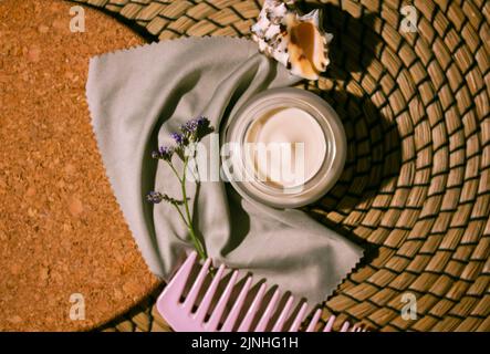 Stillleben mit Gesichtscreme im Glas, Kamm Haarbürste, lila Blumen, Muschel Draufsicht. Frauen Haut, Körper, Gesichtspflege im Sommer, Sommerferien, Stockfoto