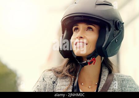 Sehen Sie die Welt als das, was sie wirklich ist, wunderschön. Nahaufnahme einer attraktiven jungen Frau, die einen Helm trägt und mit ihrem Roller durch die Stadt fährt. Stockfoto